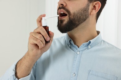 Young man using throat spray indoors, closeup