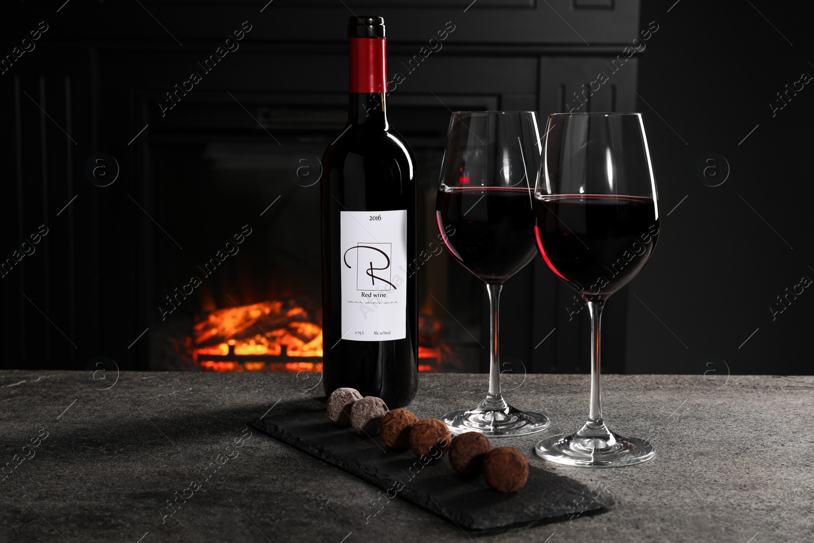 Photo of Red wine and chocolate truffles on gray table against fireplace, space for text