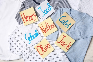 Many sticky notes with different baby names on child's clothes, flat lay