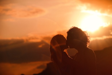 Photo of Young woman in bikini kissing her boyfriend on beach at sunset. Lovely couple