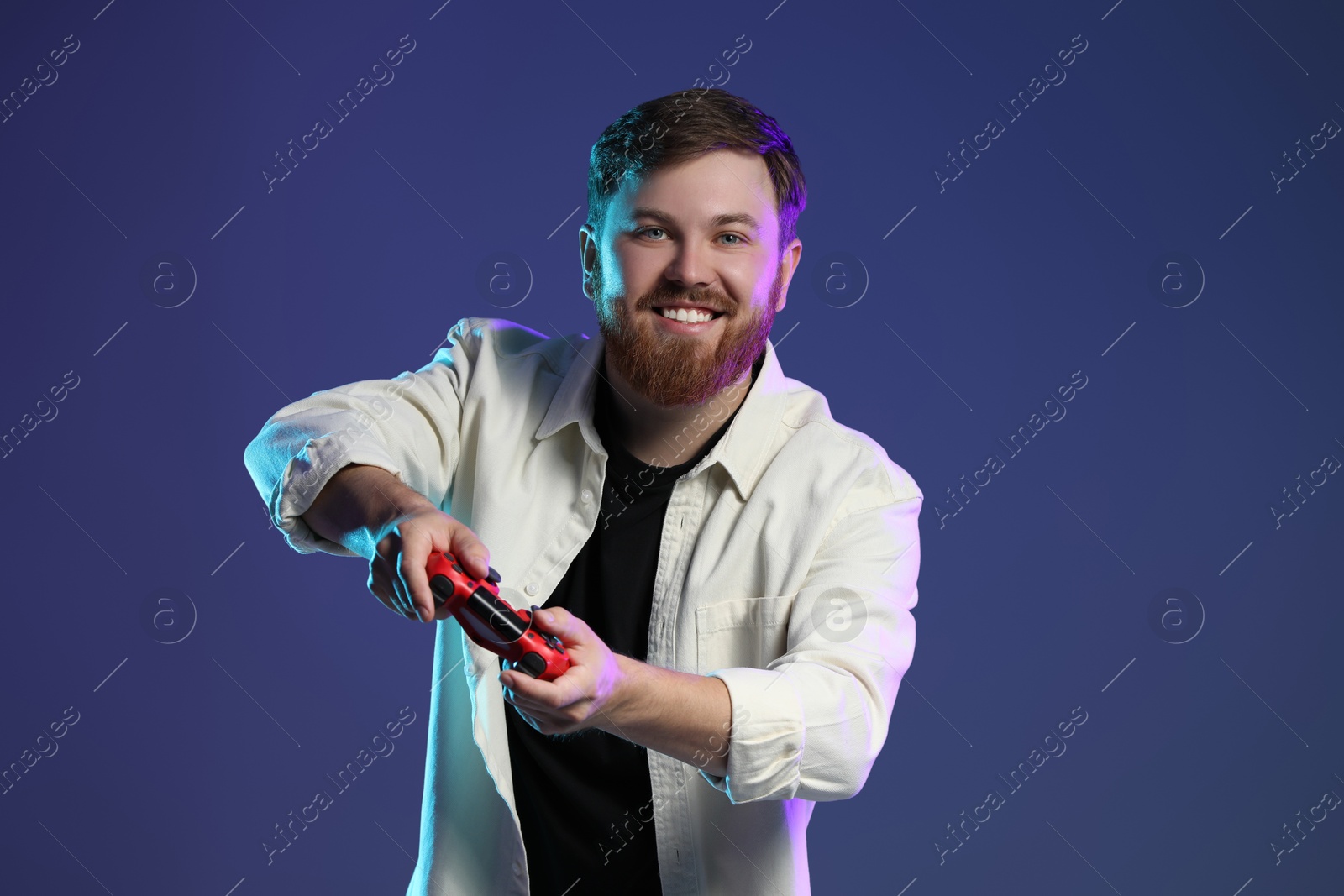 Photo of Happy man playing video game with controller on dark blue background