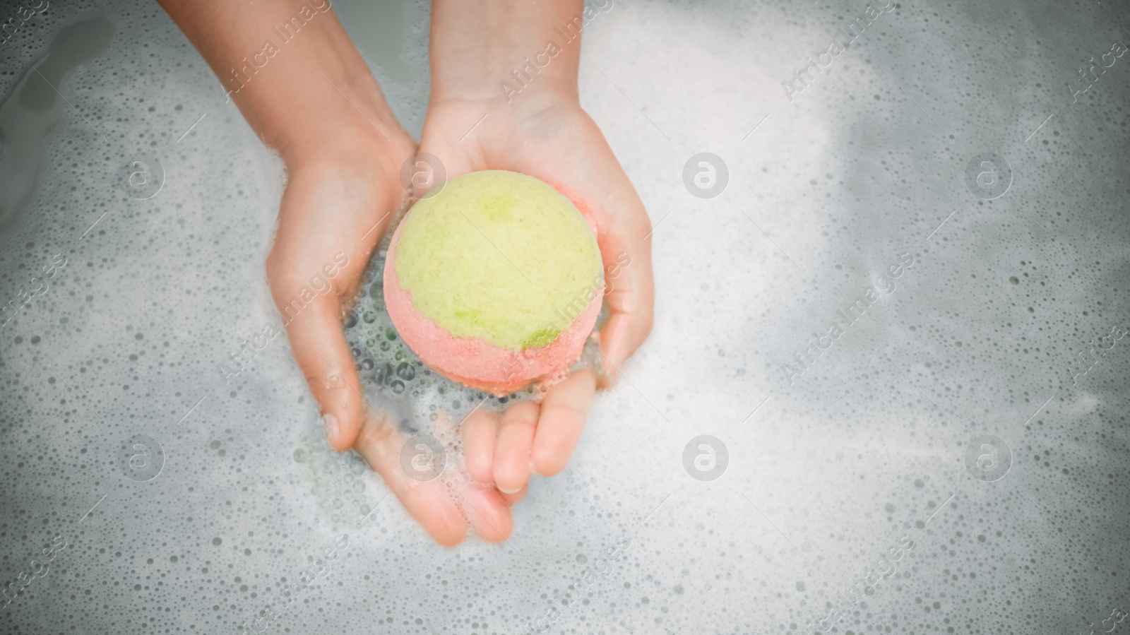 Photo of Woman holding bath bomb over water with foam, top view. Space for text