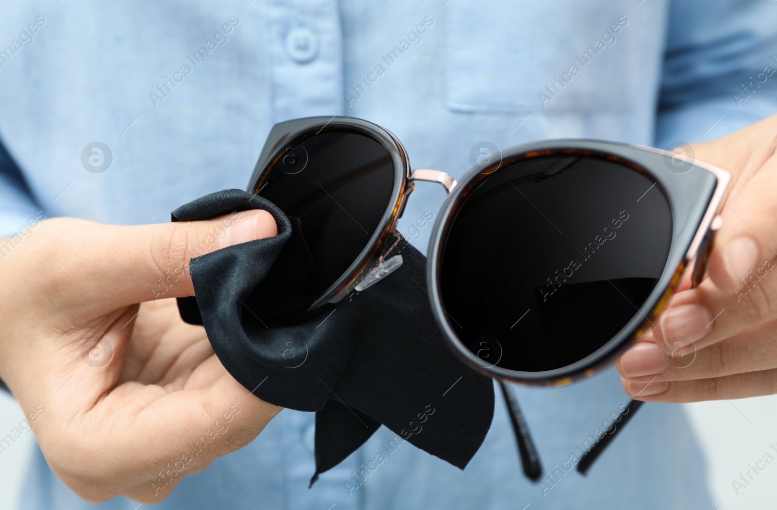 Photo of Woman wiping sunglasses with microfiber cleaning cloth, closeup