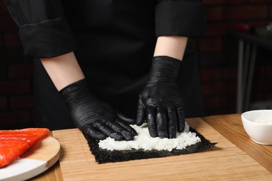 Photo of Chef in gloves making sushi roll at wooden table, closeup