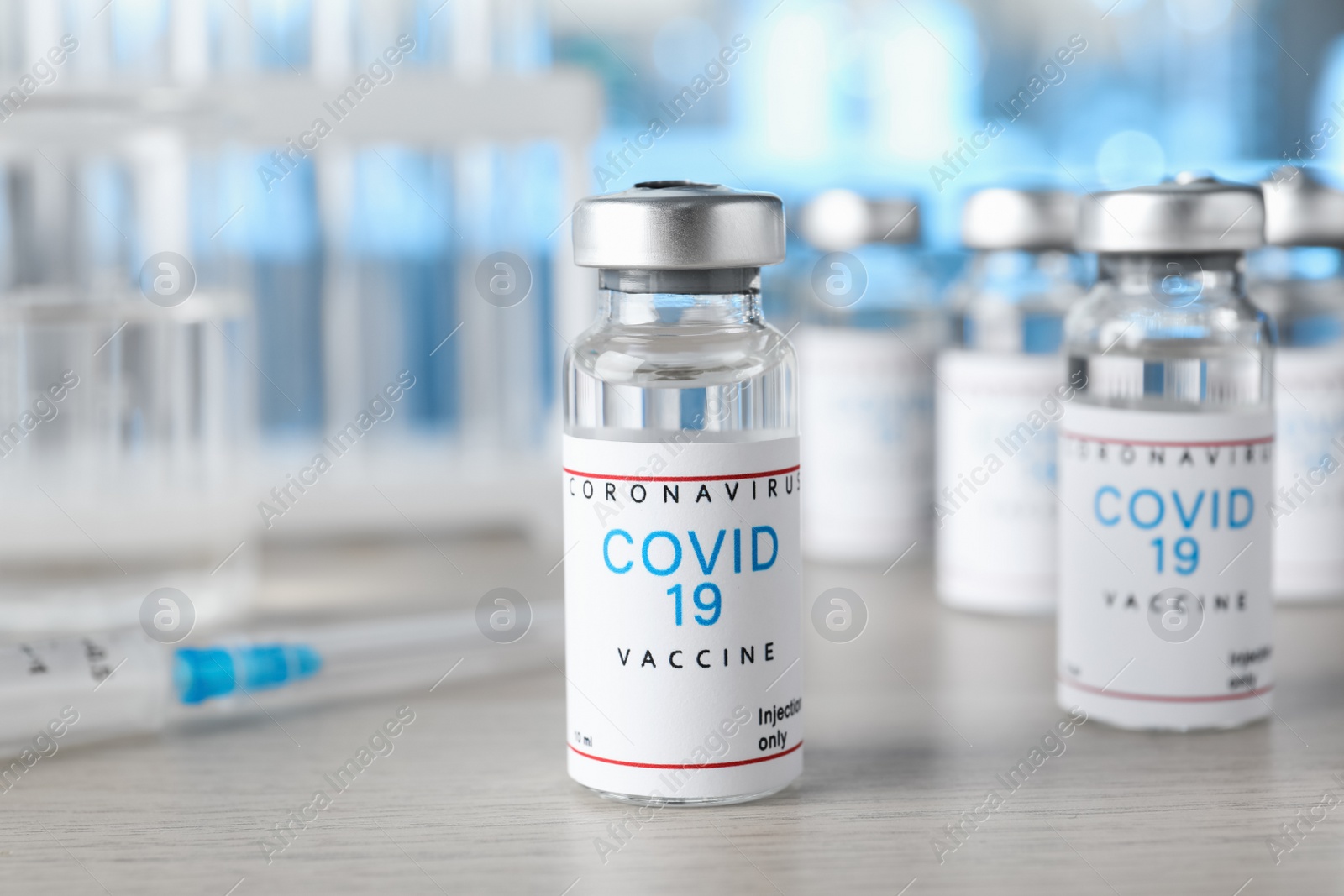 Photo of Glass vials with COVID-19 vaccine on wooden table