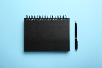 Notebook and pen on light blue background, top view