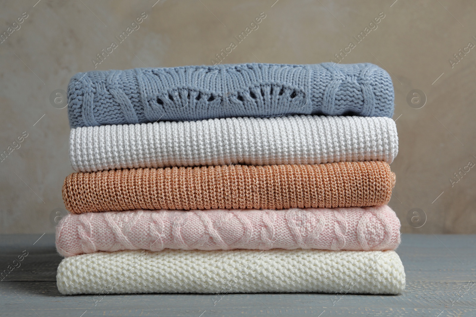 Photo of Stack of warm clothes on wooden table against grey background. Autumn season