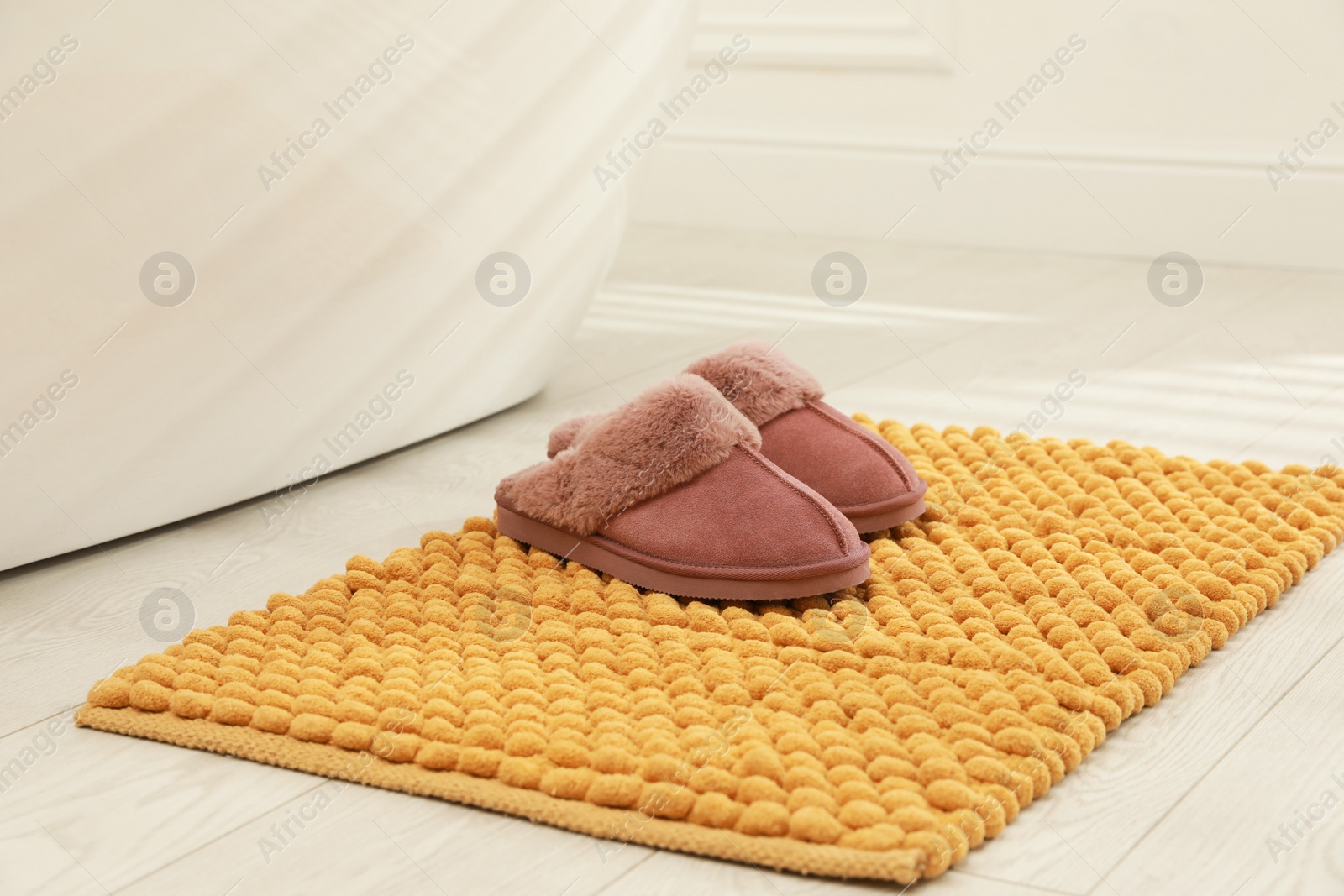 Photo of New yellow bath mat with soft slippers near tub indoors