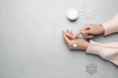 Photo of Woman applying cream onto hand on light grey table, top view. Space for text