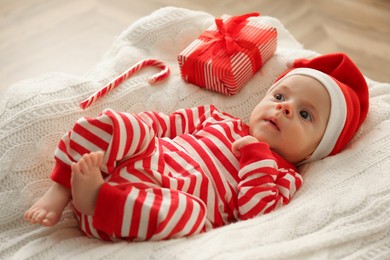 Cute little baby wearing Christmas hat on knitted blanket indoors
