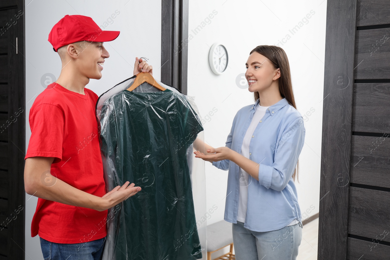 Photo of Dry-cleaning delivery. Courier giving dress in plastic bag to woman indoors