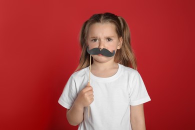 Photo of Emotional little girl with fake mustache on red background