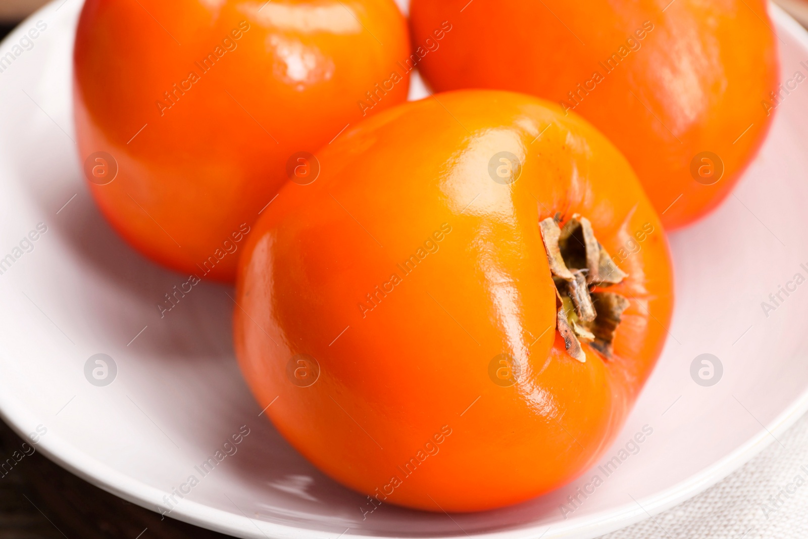 Photo of Delicious ripe persimmons in bowl on table, closeup