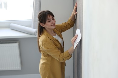 Photo of Woman smoothing stylish gray wallpaper in room