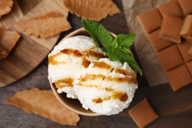 Photo of Scoops of tasty ice cream with caramel sauce and mint on wooden table, flat lay