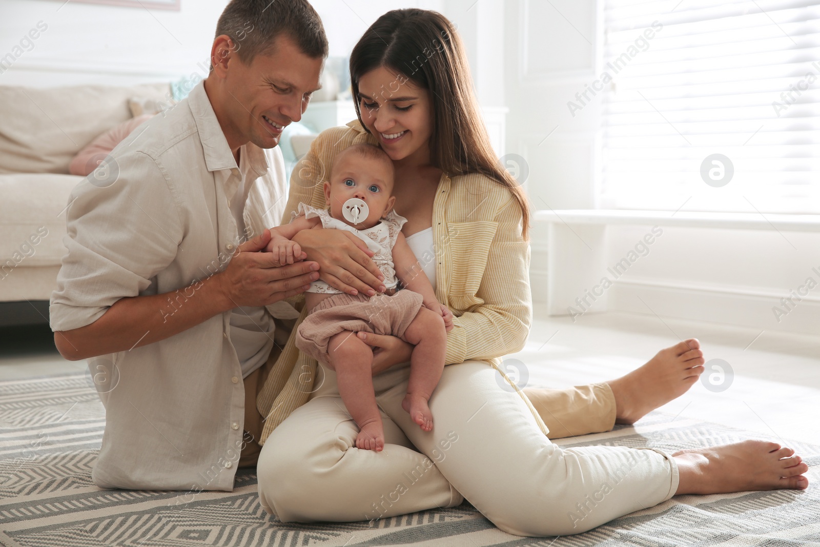 Photo of Happy couple holding their cute little baby with pacifier at home