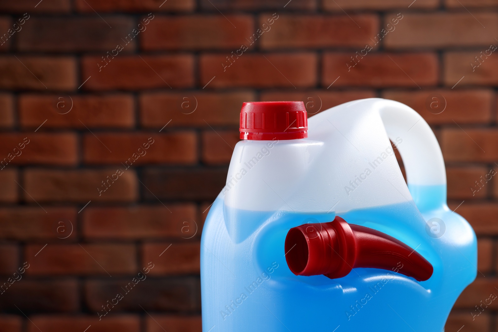 Photo of Plastic canister with blue liquid against brick wall, closeup. Space for text