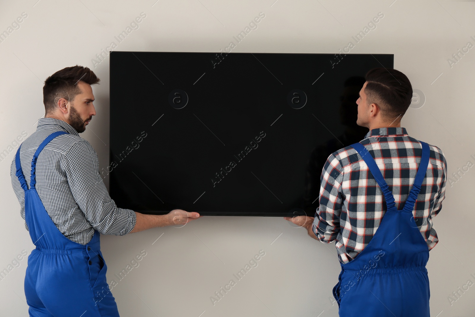 Photo of Professional technicians installing modern flat screen TV on wall indoors