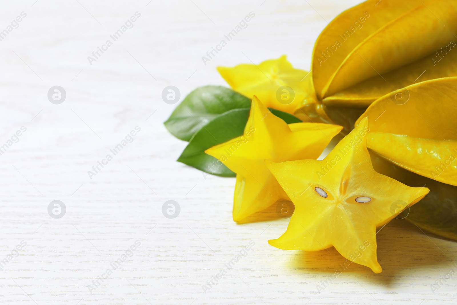 Photo of Delicious carambola fruits on white wooden table. Space for text