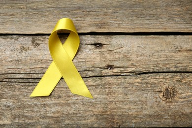 Yellow awareness ribbon on wooden table, top view. Space for text