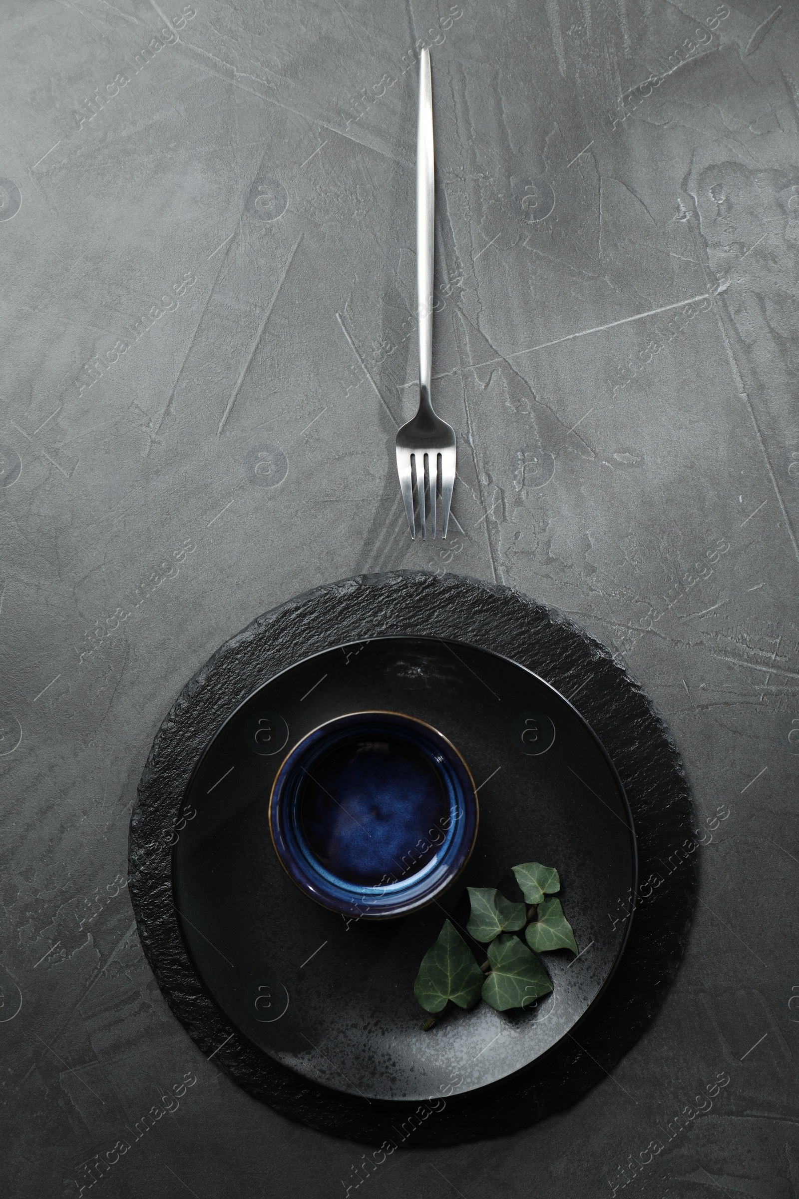 Photo of Stylish table setting. Dishes, fork and green leaves on grey surface, top view