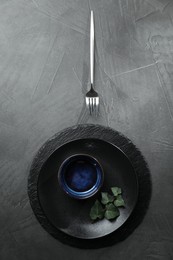 Stylish table setting. Dishes, fork and green leaves on grey surface, top view