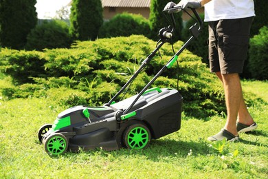 Man cutting grass with lawn mower in garden on sunny day, closeup