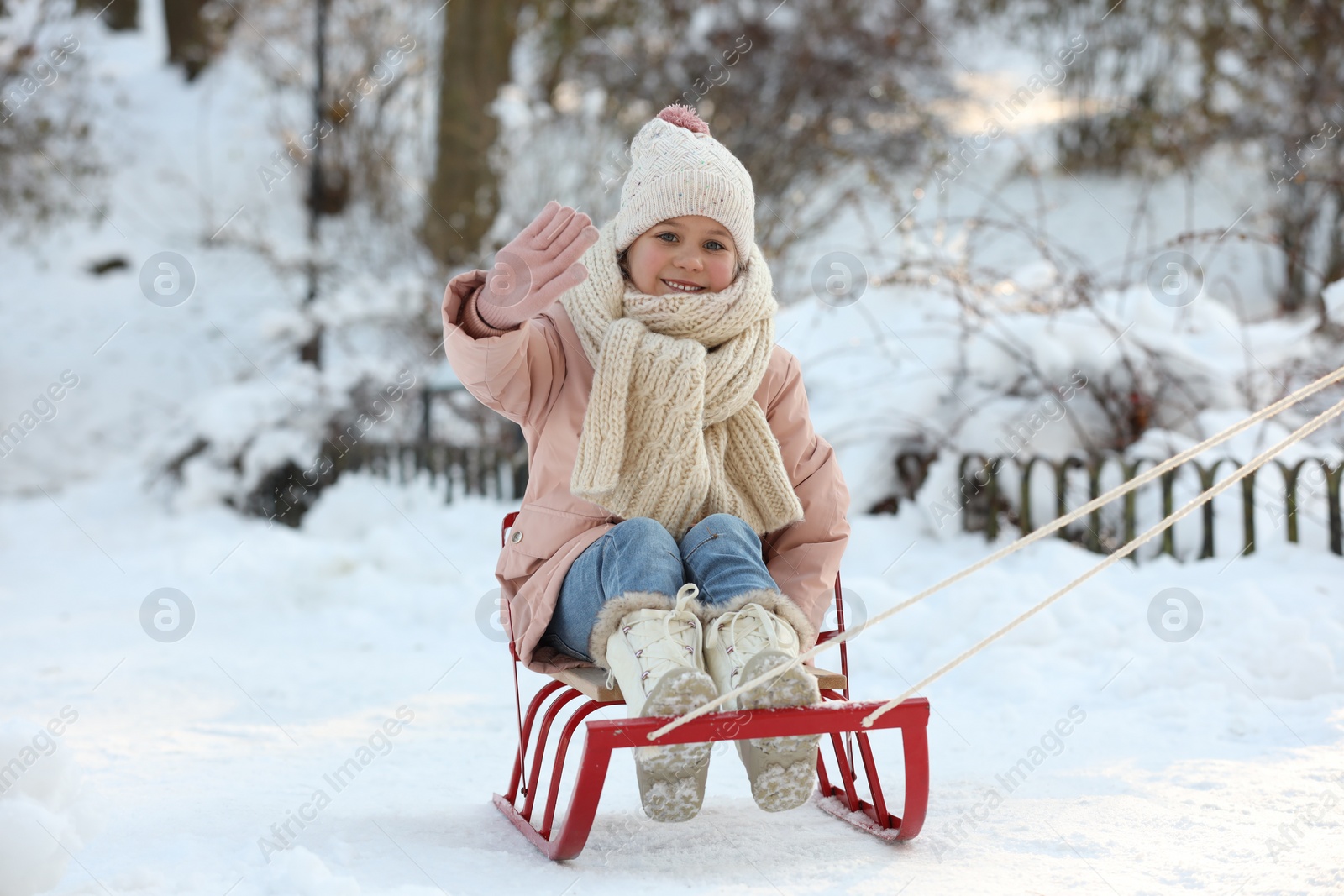 Photo of Cute little girl enjoying sledge ride through snow in winter park