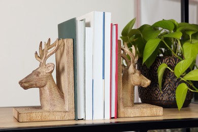 Wooden deer shaped bookends with books and plant on shelf indoors