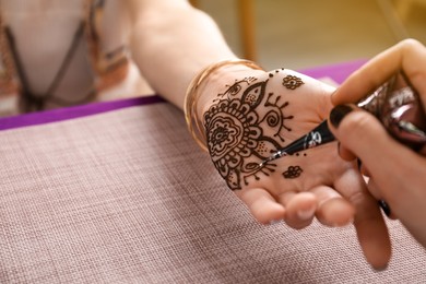 Photo of Professional mehndi master making henna tattoo at table, closeup. Space for text