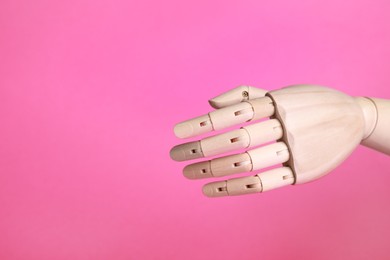 Wooden mannequin hand on pink background. Space for text