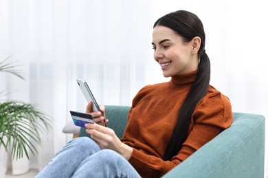 Happy young woman with smartphone and credit card shopping online on sofa at home