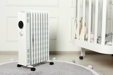 Photo of Modern portable electric heater and baby crib indoors
