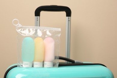 Photo of Cosmetic travel kit in plastic bag on suitcase against beige wall. Bath accessories