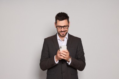 Handsome man in suit looking at smartphone on light grey background