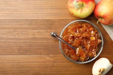 Photo of Tasty apple jam in glass bowl and fresh fruits on wooden table, flat lay. Space for text