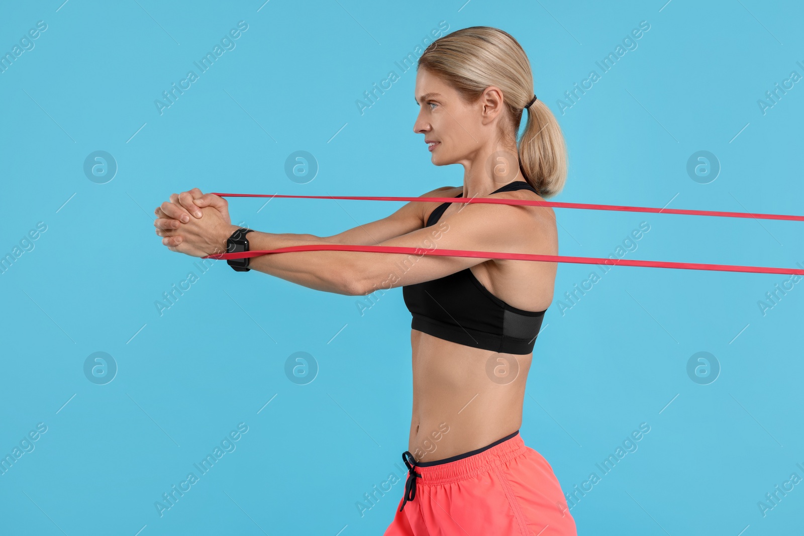 Photo of Woman exercising with elastic resistance band on light blue background