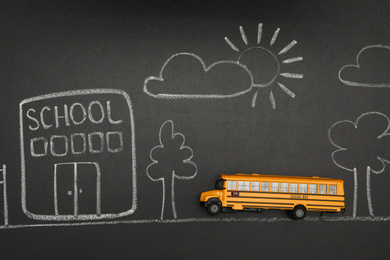 Photo of Yellow bus and drawing of school on chalkboard, top view. Transport for students