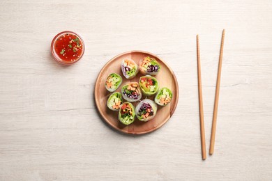 Photo of Tasty spring rolls, chopsticks and sauce on white wooden table, flat lay