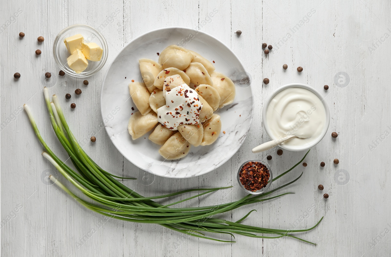 Photo of Delicious cooked dumplings with sour cream on white wooden table, flat lay