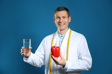 Photo of Nutritionist with glass of water and bell pepper on blue background