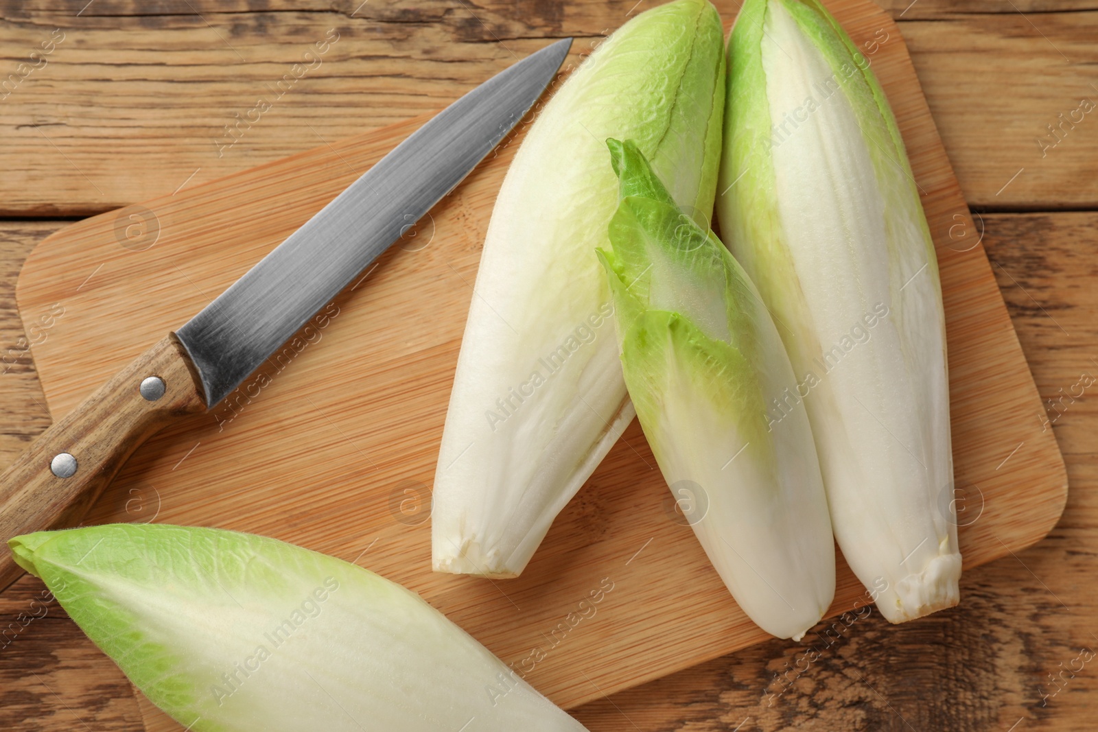 Photo of Fresh raw Belgian endives (chicory), board and knife on wooden table, top view