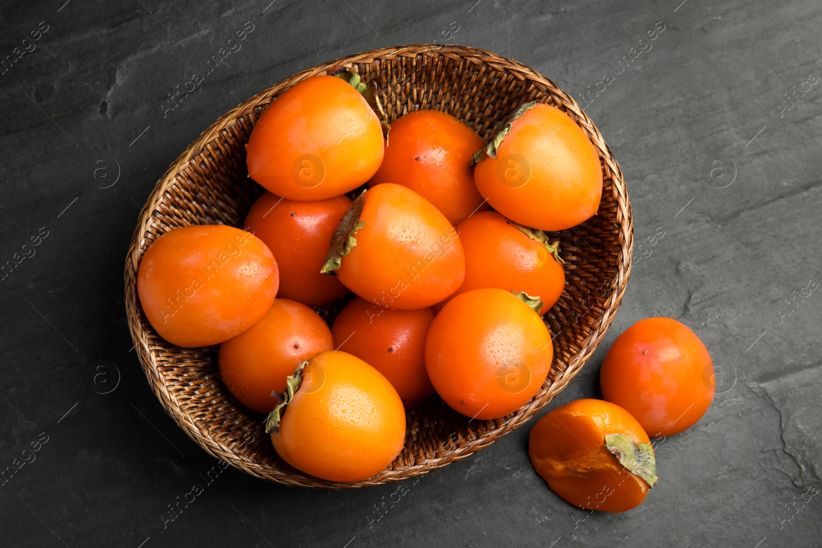 Photo of Delicious fresh persimmons on black slate table, flat lay