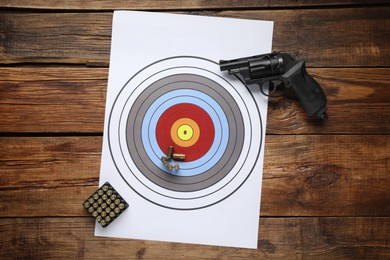 Photo of Shooting target, handgun and bullets on wooden table, top view