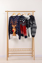 Rack with different Christmas sweaters near white wall