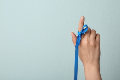 Photo of Woman with blue ribbon on finger against light background, closeup. Symbol of social and medical issues