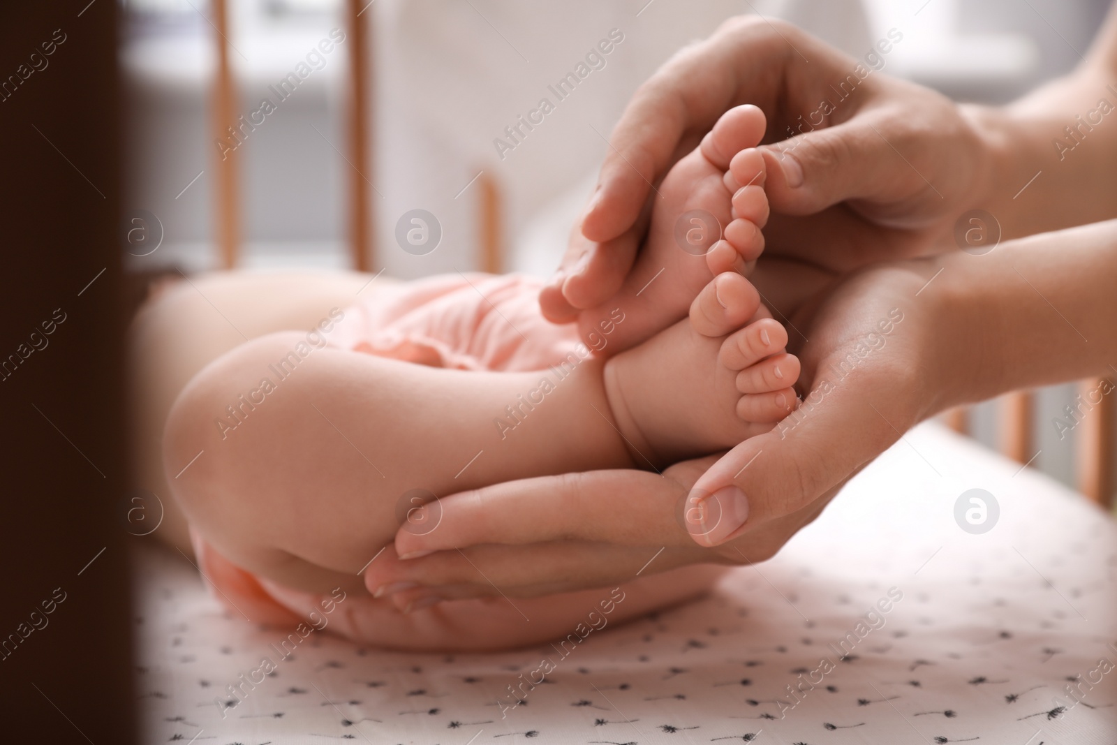 Photo of Mother holding feet of her cute sleeping baby at home, closeup