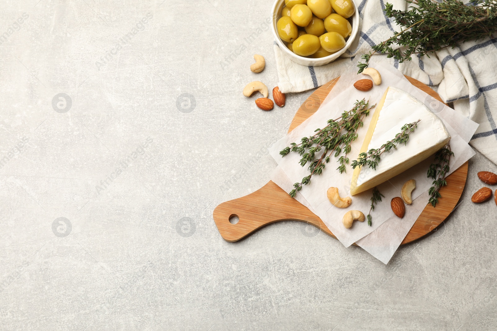 Photo of Piece of tasty camembert cheese, thyme, nuts and olives on grey textured table, flat lay. Space for text