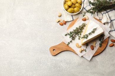 Piece of tasty camembert cheese, thyme, nuts and olives on grey textured table, flat lay. Space for text