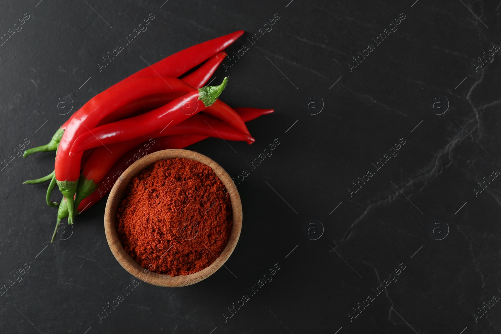 Photo of Paprika powder and fresh chili peppers on black table, flat lay. Space for text